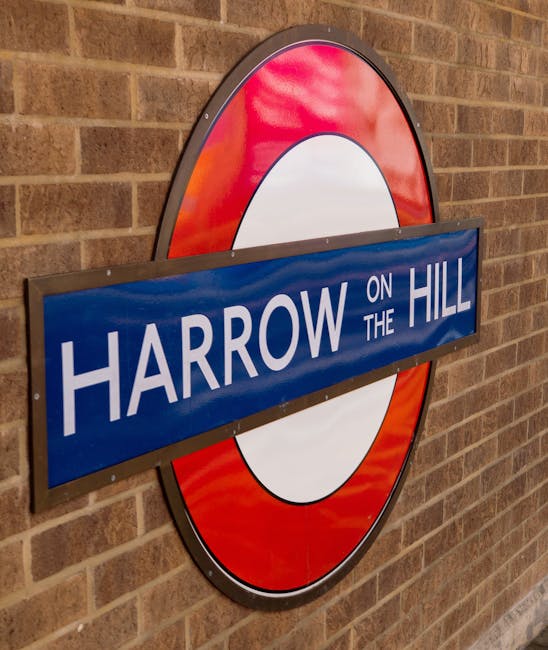 A view from a low angle inside a London underground station, focusing on the platform edge with a textured, grooved surface in brown and yellow warning lines running along the center. The curved tunnel walls are lined with white, grey, and black tiles arching overhead, illuminated by long strip lighting. Along the station walls, there are several large advertising posters, one promoting a mobile phone network and others displaying fashion and entertainment content, framed by yellow and silver trim. Passengers are seated on benches and standing, waiting for trains, with some visible in the background near the platform's edge. The environment appears clean, well-lit, and organized, characteristic of an urban transit station used by commuters. The setting conveys a typical underground station environment, emphasizing the safety markings and commercial advertisements common in London's public transport system, representative of private or independent railway station services. Waste Disposal Stockwell's rubbish removal services catering to urban environments could be inferred as part of maintaining such high-traffic public spaces, although not directly depicted in the image.